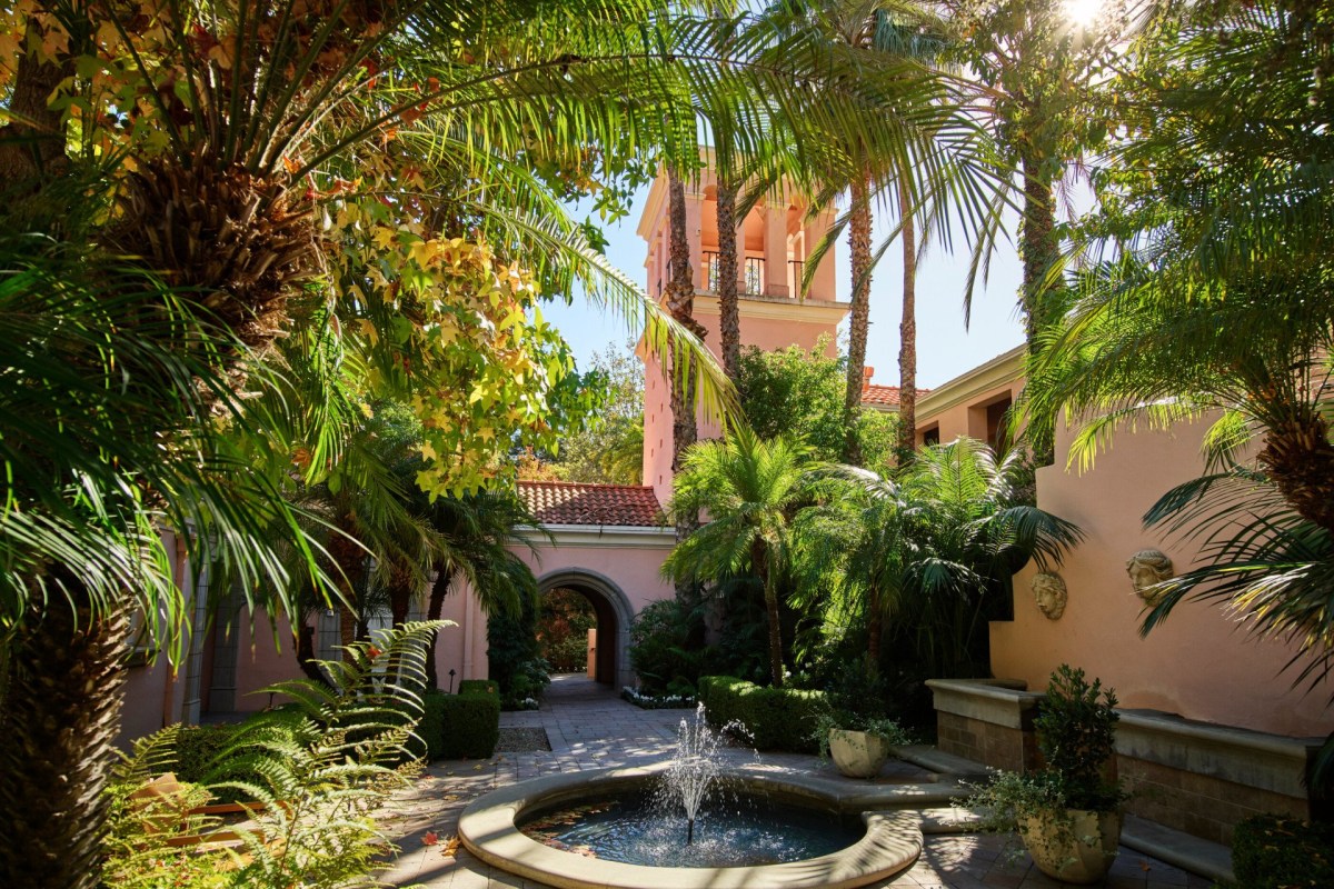 Hotel Bel-Air courtyard with stone fountain, palm trees, and pink tower building in background