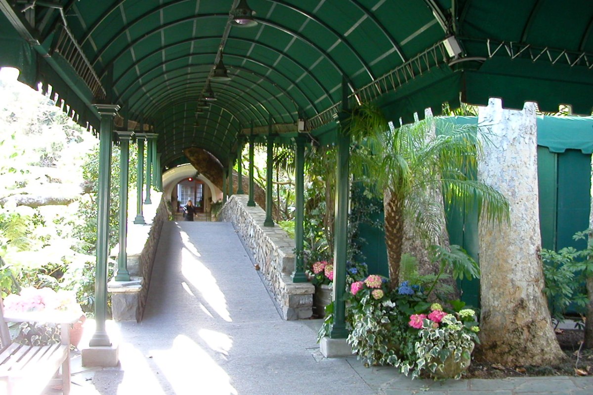Covered garden walkway entrance with green canopy, stone path, and flowering plants
