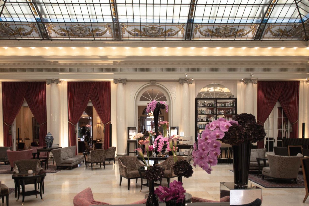 Elegant hotel lobby with glass skylight, red curtains, marble floor and orchid arrangements