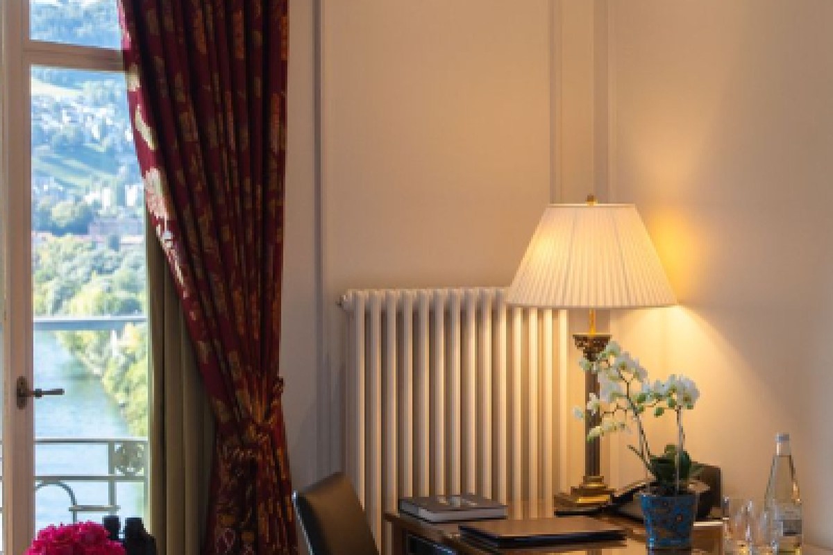 Guest room corner with lamp, orchid, desk and view of river and hills through curtains