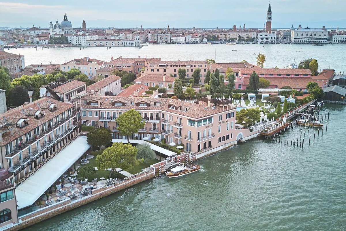 Aerial view of Hotel Cipriani's waterfront façade and gardens along the Venice lagoon with the city skyline beyond