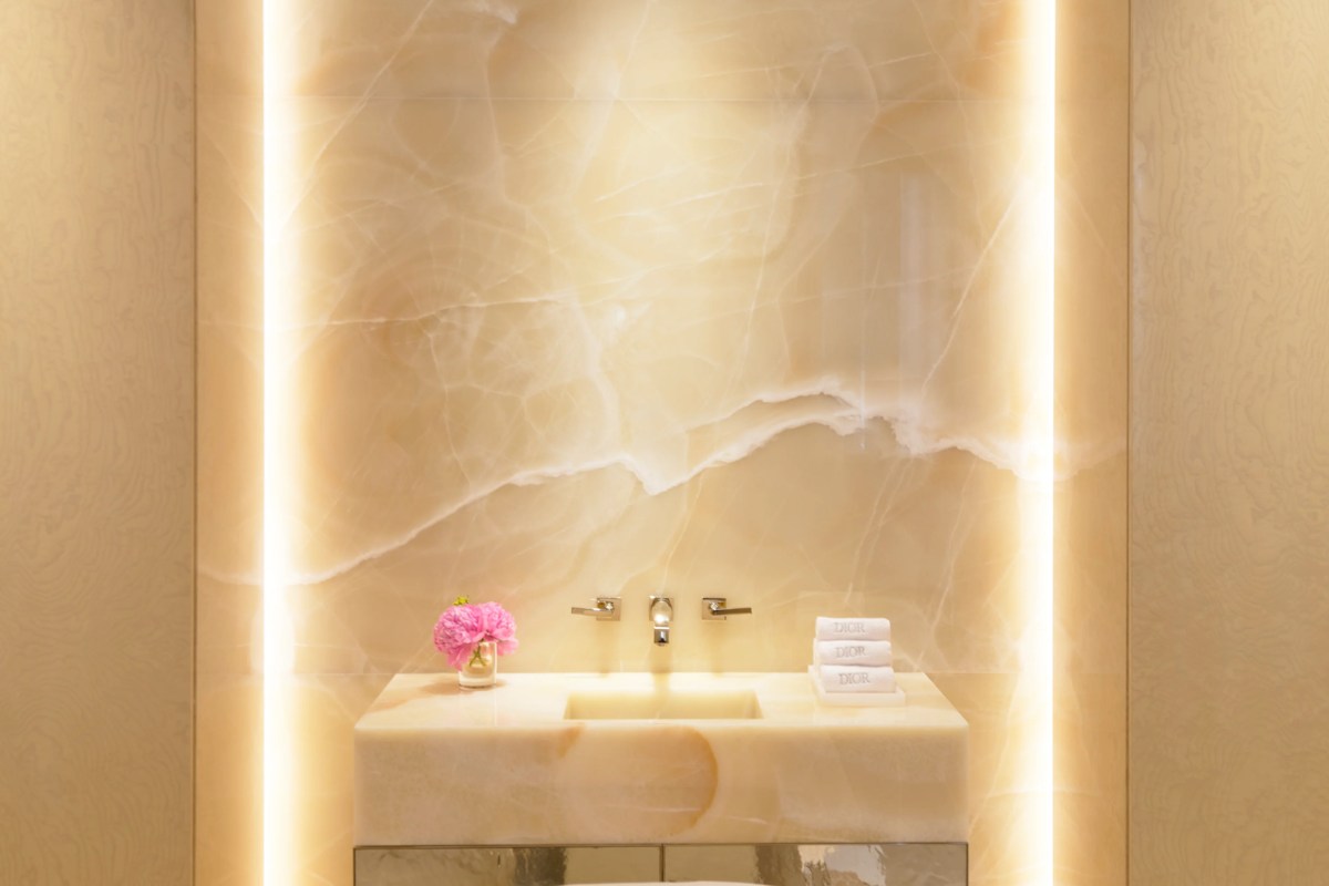 Luxury marble bathroom vanity with backlit onyx wall, flowers, and folded Dior towels