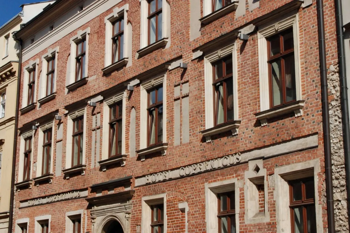 Close-up angled view of Hotel Copernicus red brick facade with ornate stone window frames and carved signage