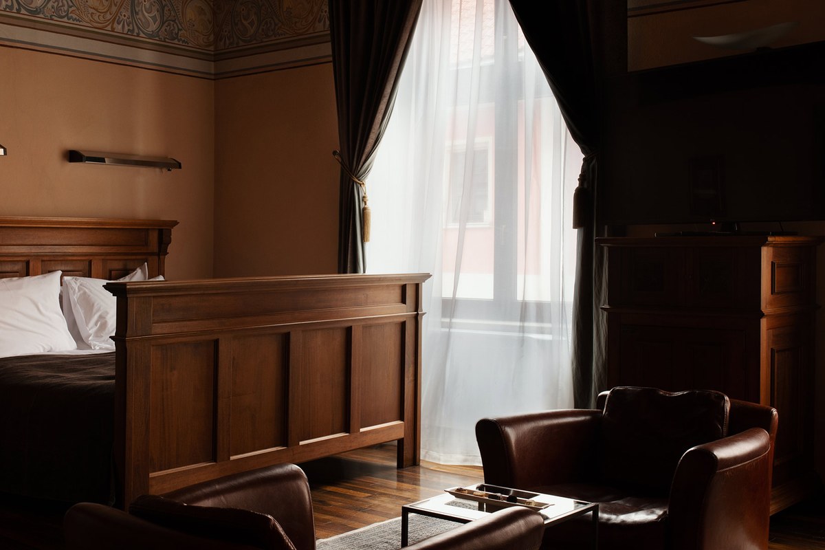 Elegant guest room with carved wooden bed frame, leather armchairs and sheer curtained window