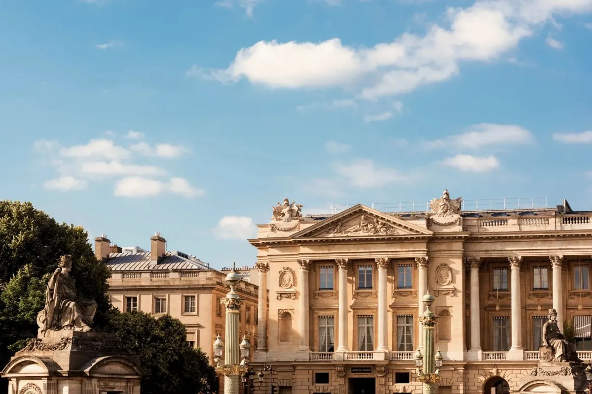 Daytime view of Hôtel de Crillon's classical stone façade with columns, under a blue sky with statues in foreground.