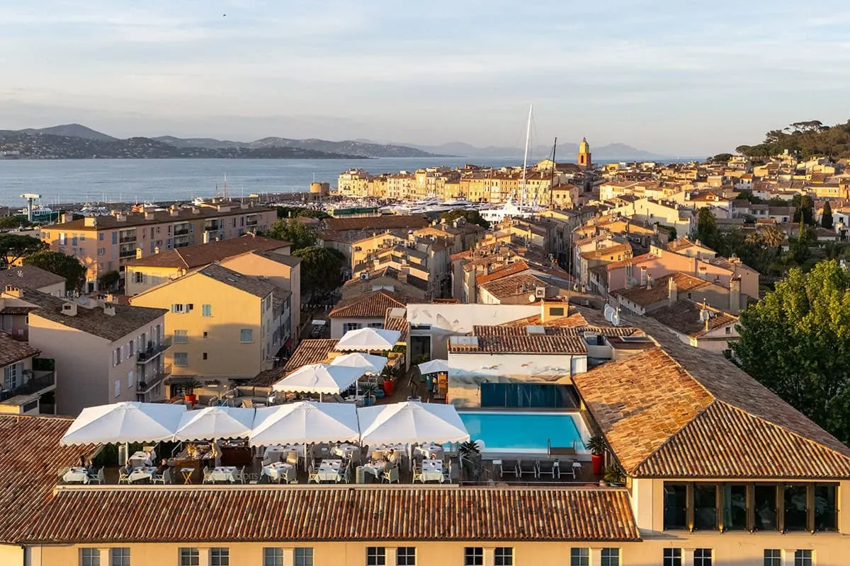 Aerial view of the hotel rooftop pool and terrace with white umbrellas, overlooking Saint-Tropez at sunset