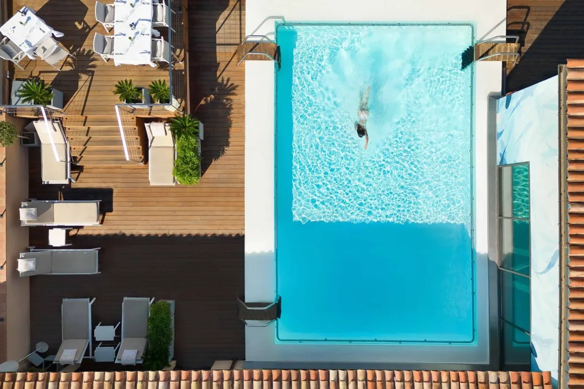 Overhead view of a rooftop swimming pool with a swimmer, surrounded by wooden deck and loungers