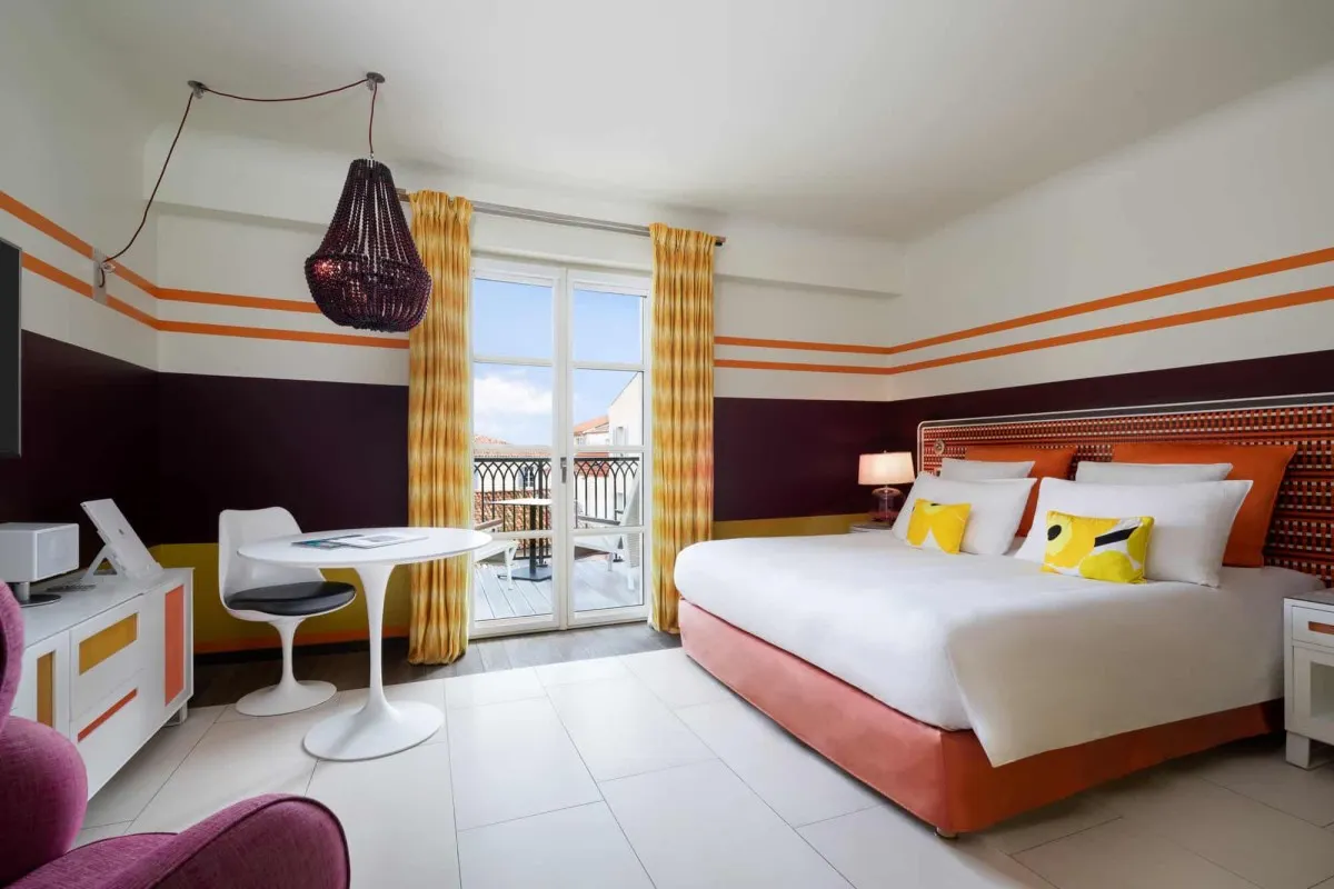 Colorful hotel bedroom with orange and purple striped walls, bed, chandelier, and balcony access