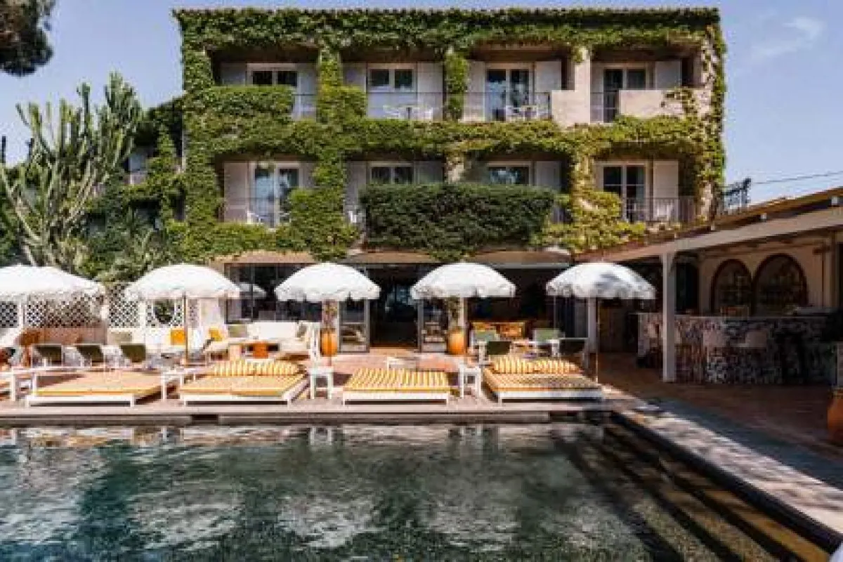 Ivy-covered hotel façade with pool, umbrellas and sun loungers in foreground