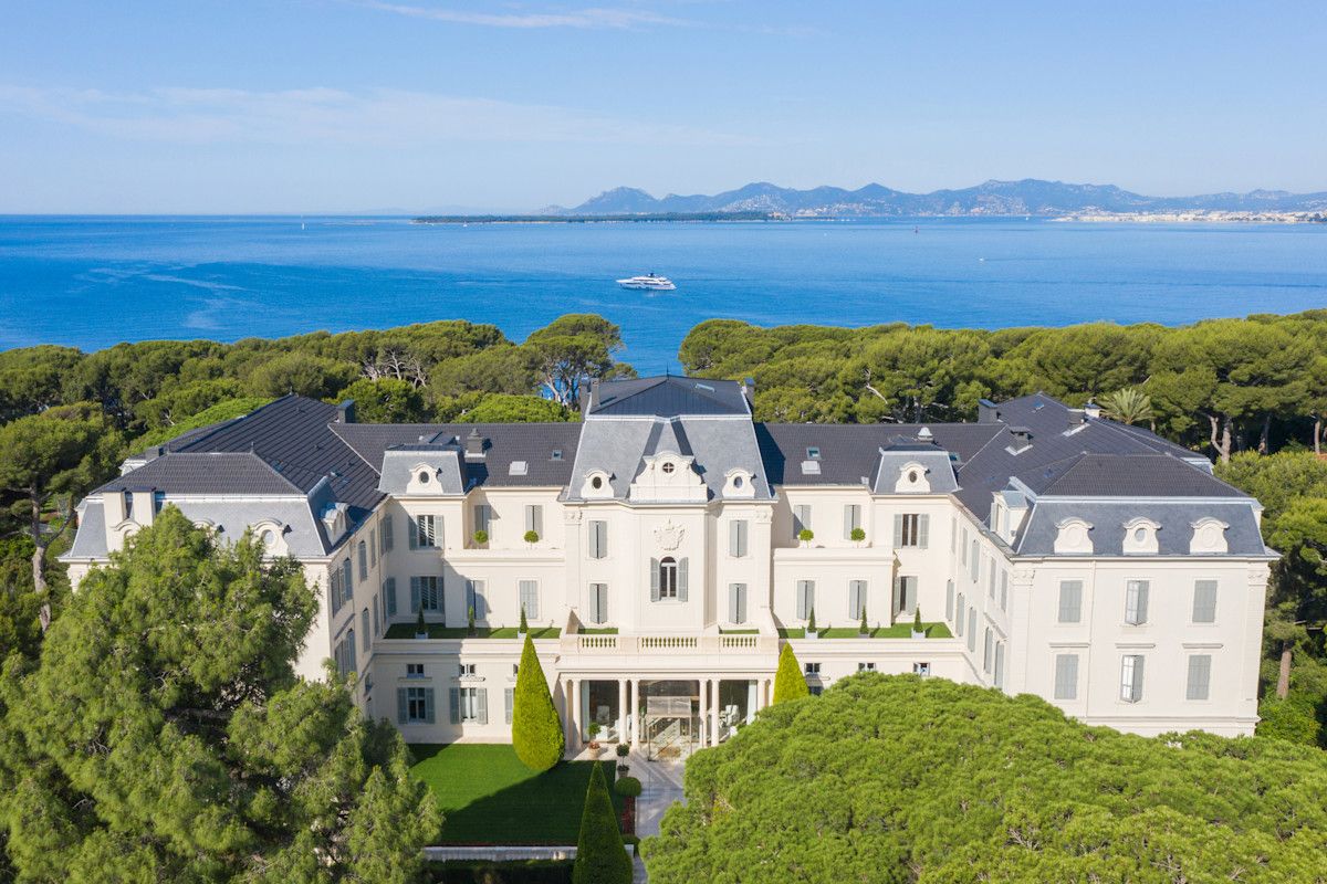 Aerial view of the white Napoleon III façade of the Hôtel du Cap-Eden-Roc among umbrella pines, with the Mediterranean behind