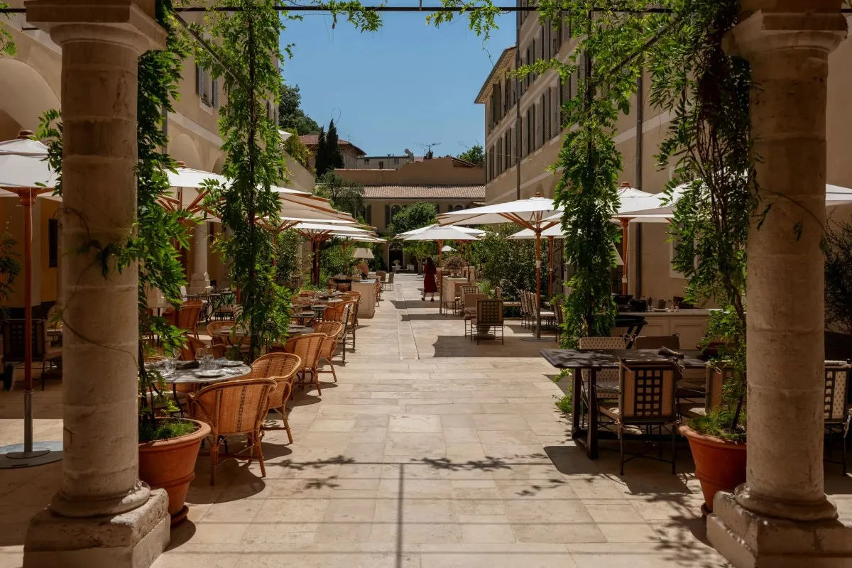 Stone courtyard with pergola and outdoor dining tables at Hotel du Couvent, with hotel building in background