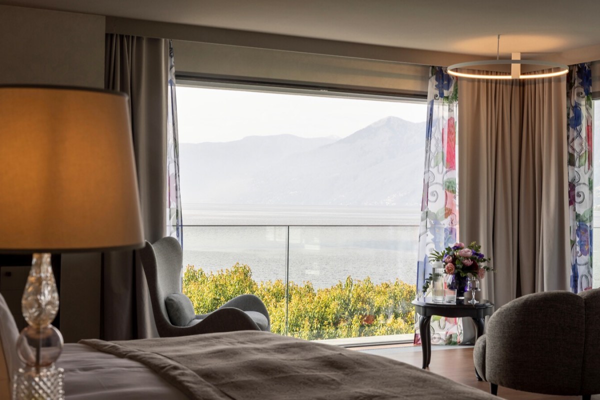 Hotel guest room interior with a bed and large window showing a lake and mountain view