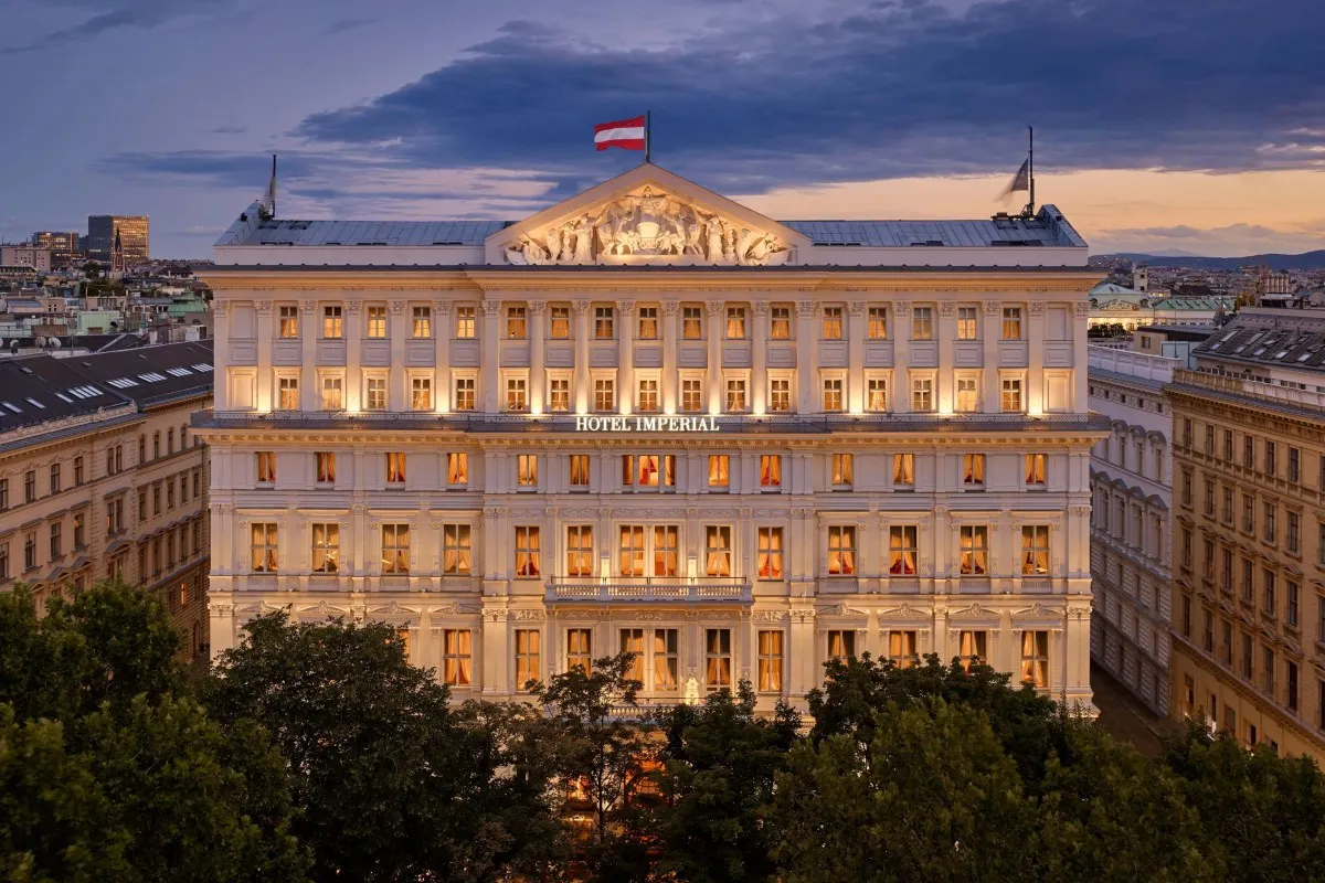 Hotel Imperial in Vienna at dusk – the floodlit Neo-Renaissance façade on the Kärntner Ring with a sculpted pediment and the Austrian flag on the roof
