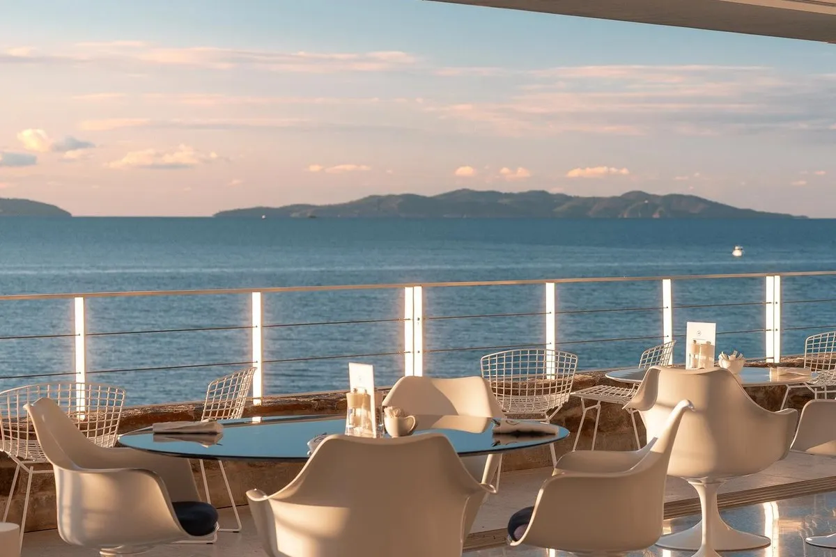 White chairs and laid tables on a terrace at Hôtel Les Roches in Le Lavandou, facing the sea and the Îles d'Or at dusk