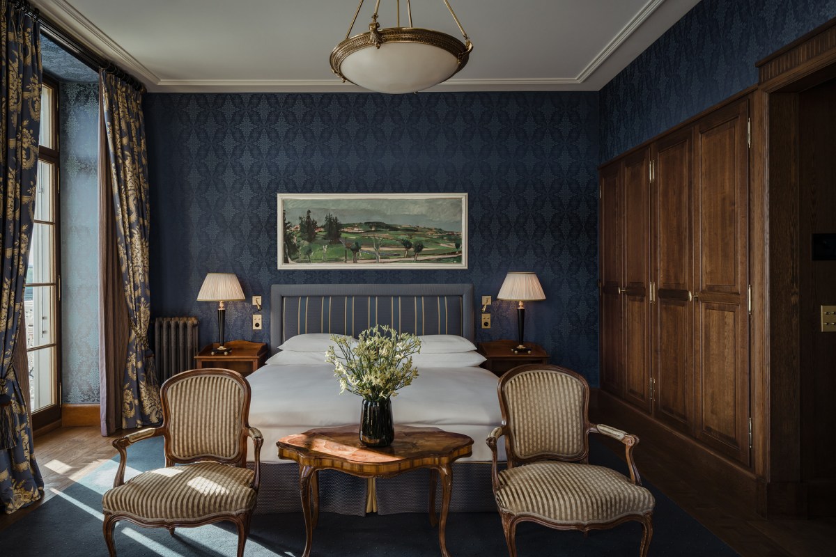 Classic guest room with navy patterned wallpaper, antique armchairs and dark wood wardrobe