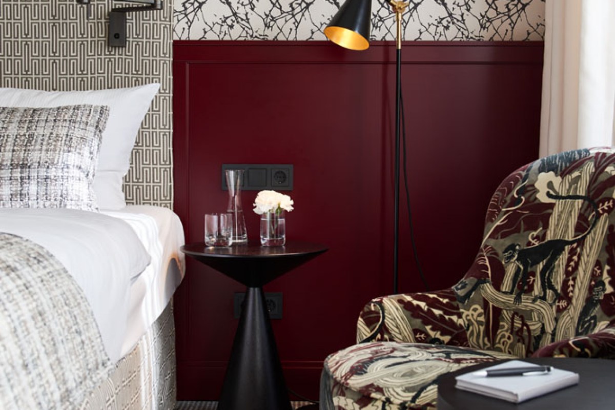 Close-up of guest room bedside table with lamp, patterned armchair and burgundy wall panel