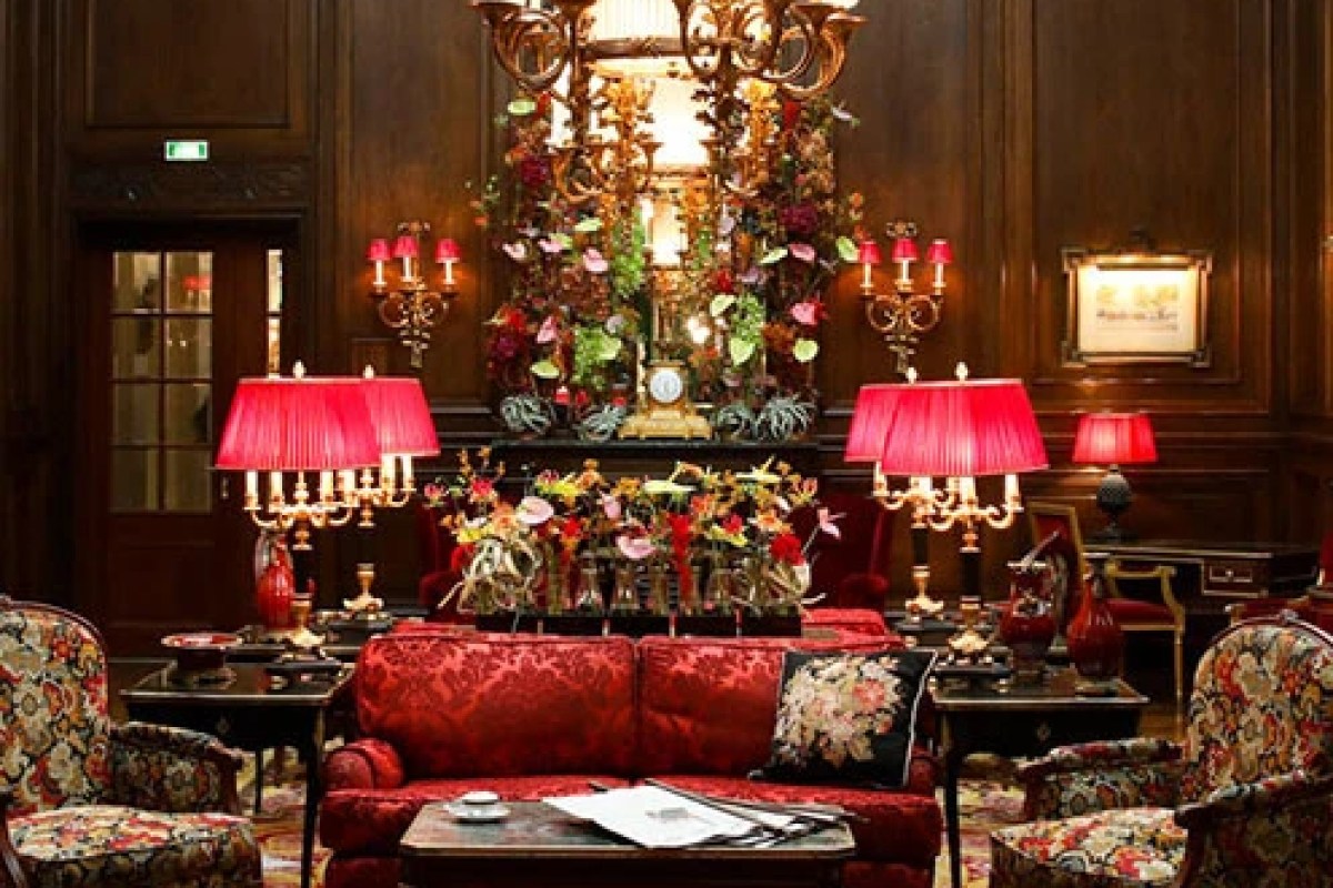 Opulent wood-paneled lounge with red sofas, candelabra lamps, and floral arrangement