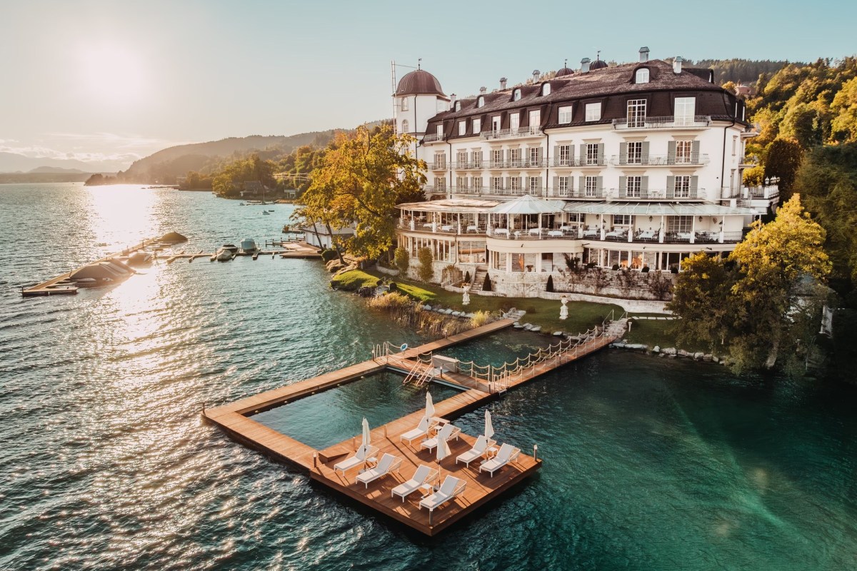 Aerial view of Hotel Schloss Seefels castle facade on the lake shore with a floating wooden pool deck at sunset