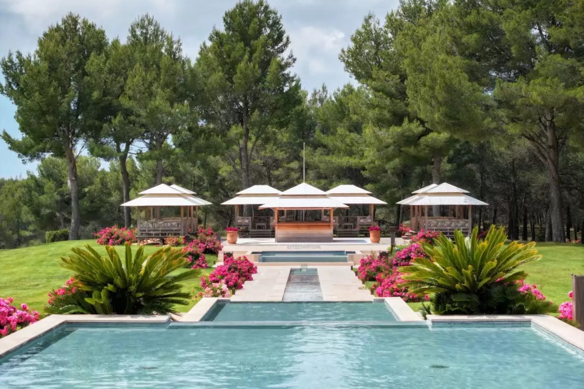Hotel pool and garden with pavilion cabanas framed by pine trees and pink flowering shrubs