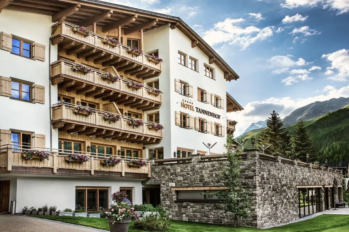 Exterior facade of Hotel Tannenhof with wooden balconies, flower boxes, stone wall and mountain backdrop
