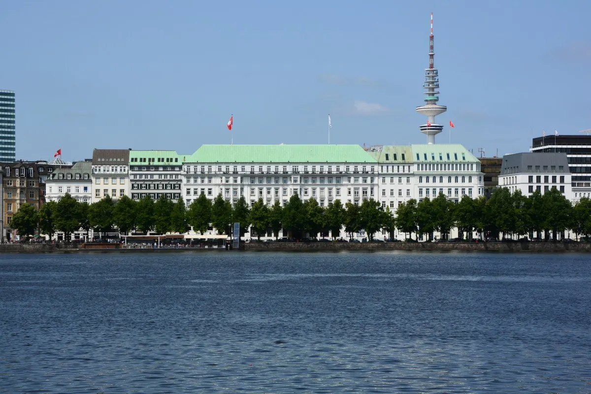 Hotel Vier Jahreszeiten's green-roofed facade seen across the Alster lake with the TV tower behind