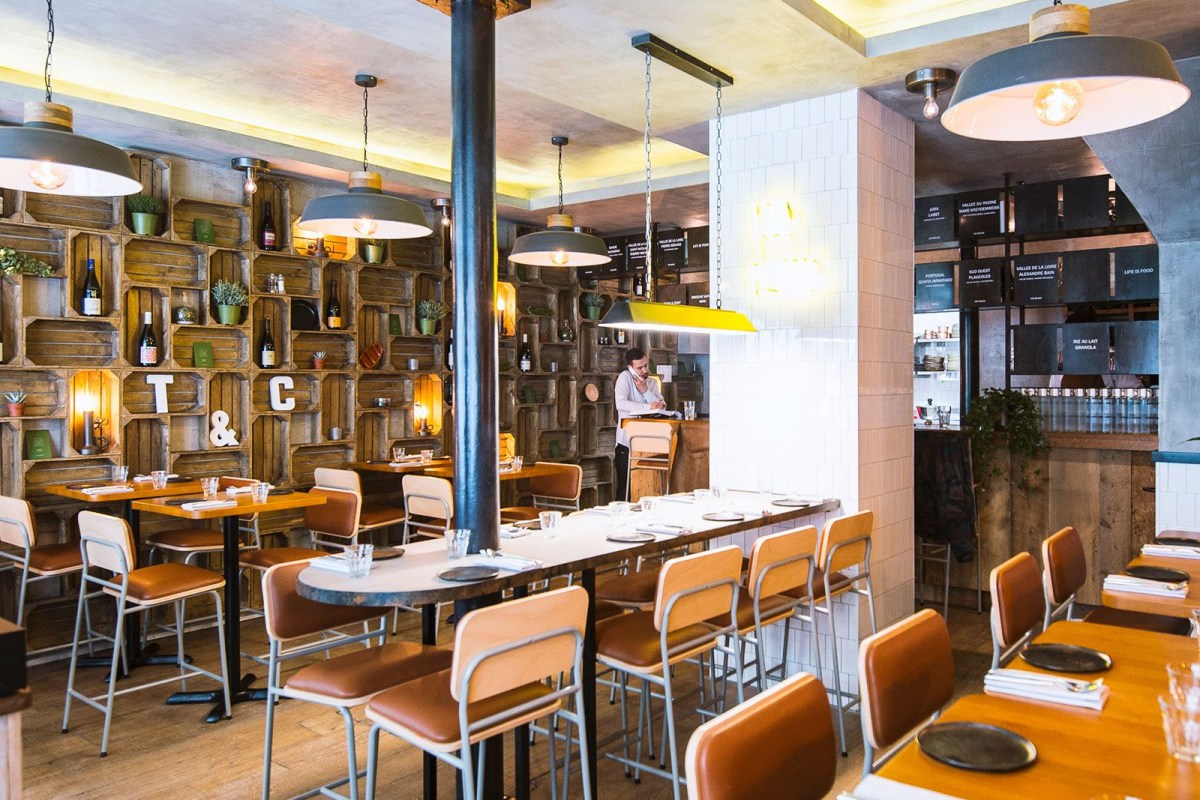 Dining room view with crate wall shelving, pendant lights, and staff member near bar