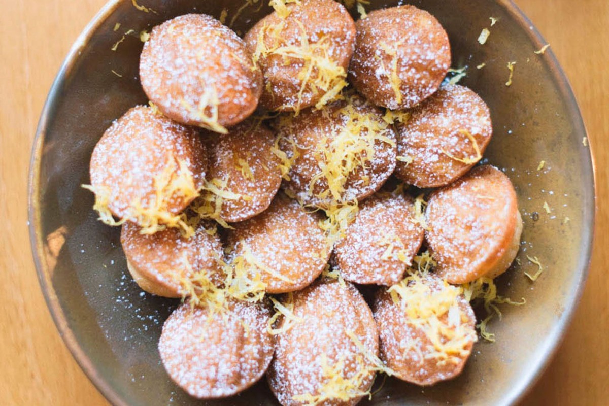 Plate of madeleines dusted with powdered sugar and lemon zest on a wooden table