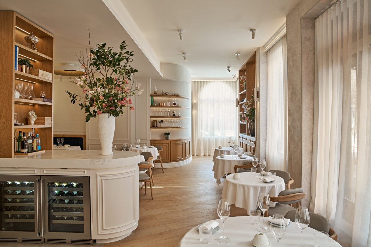 Elegant dining room with white tablecloths, floral arrangement, and wine fridge at bar counter