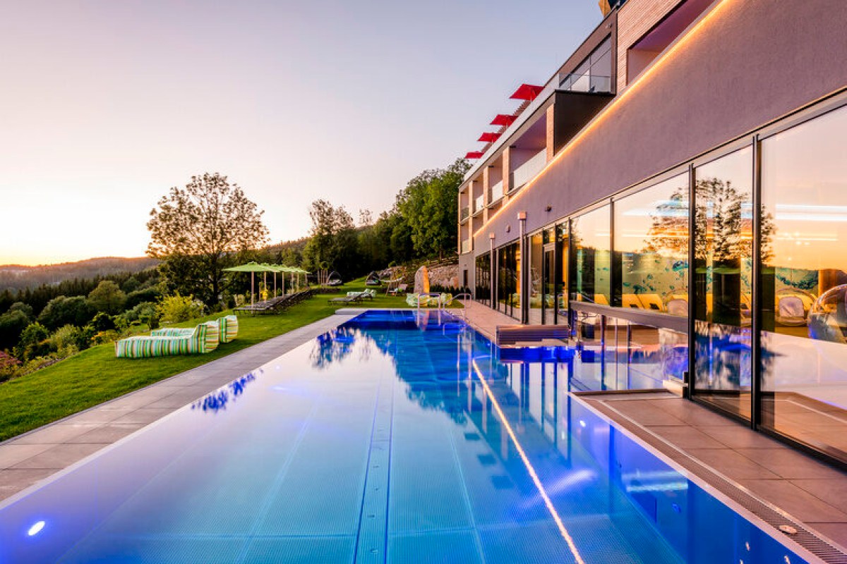 Hotel exterior at dusk with infinity pool, terrace loungers and garden view