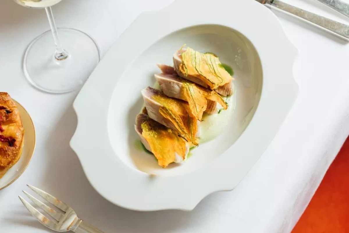 Plated fish dish with fried squash blossoms on white oval plate at a laid table