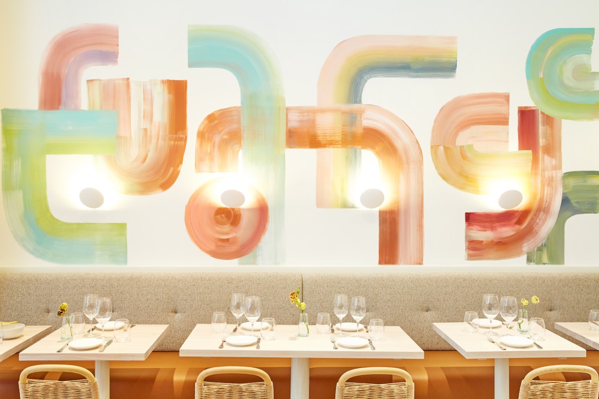 Dining room wall with pastel abstract mural above set tables with wine glasses and rattan chairs