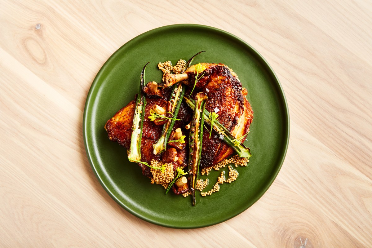 Overhead shot of roasted chicken with charred okra and mustard seeds on a green plate