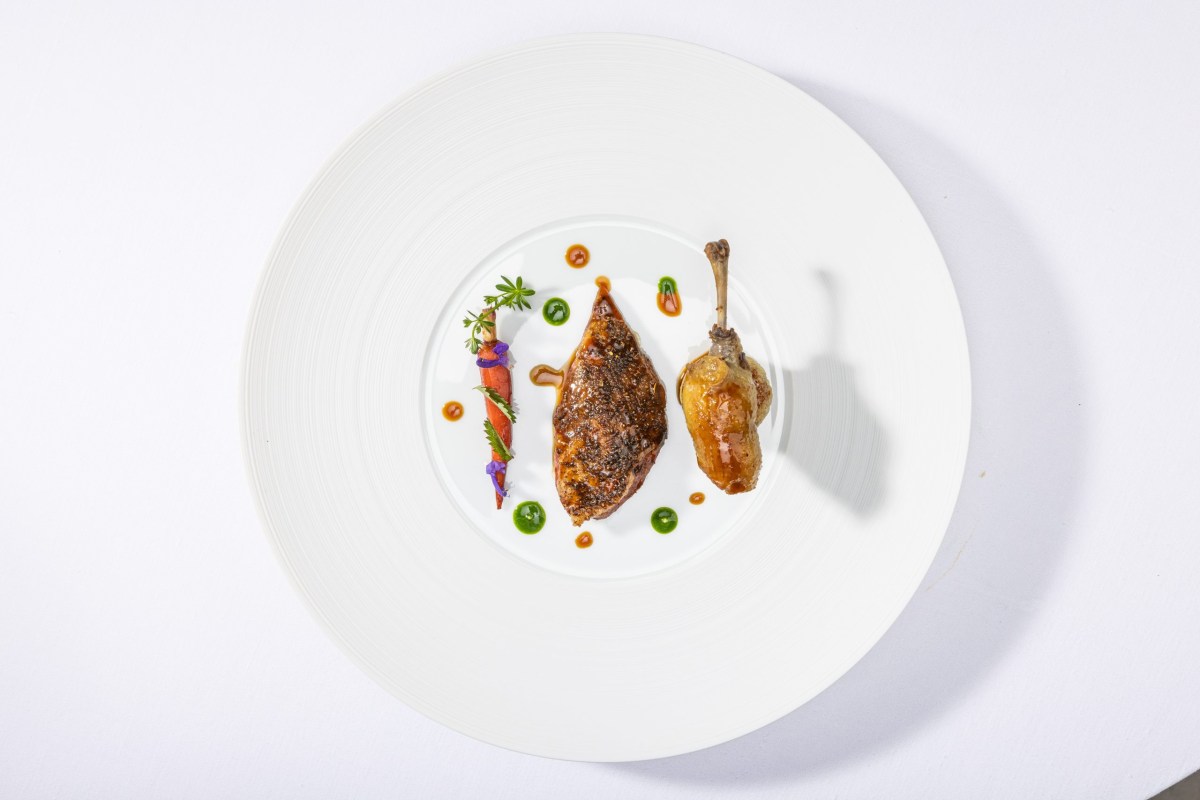 Overhead shot of a white plate with seared duck breast, confit leg, and glazed carrot garnish