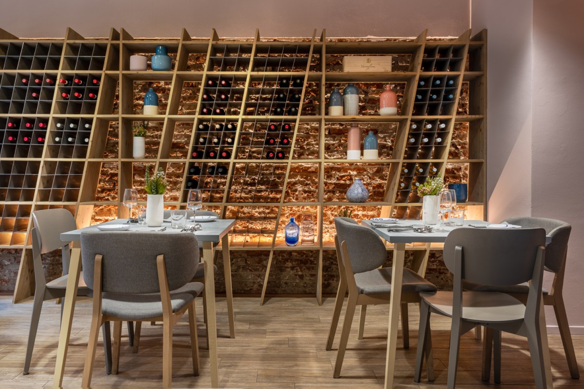 Restaurant dining room with wine storage wall, wooden tables set for dining, and grey upholstered chairs