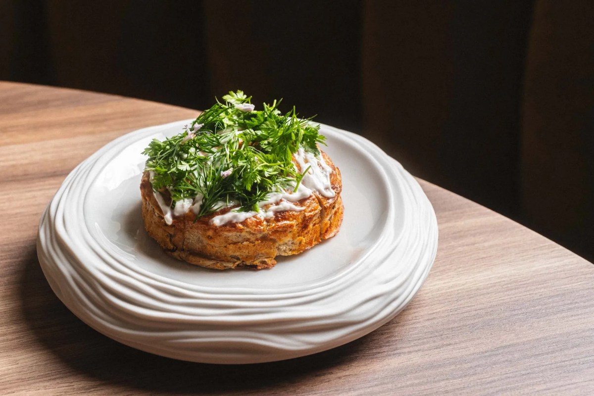 A round plate holding a crispy baked dish topped with fresh herbs, served on a wooden table.