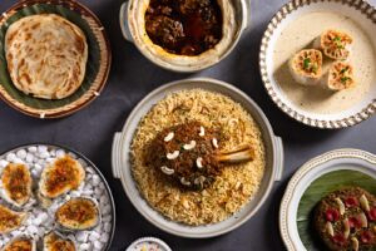 Overhead spread of multiple Indian dishes including naan, lamb rajma, biryani and oysters on a dark table