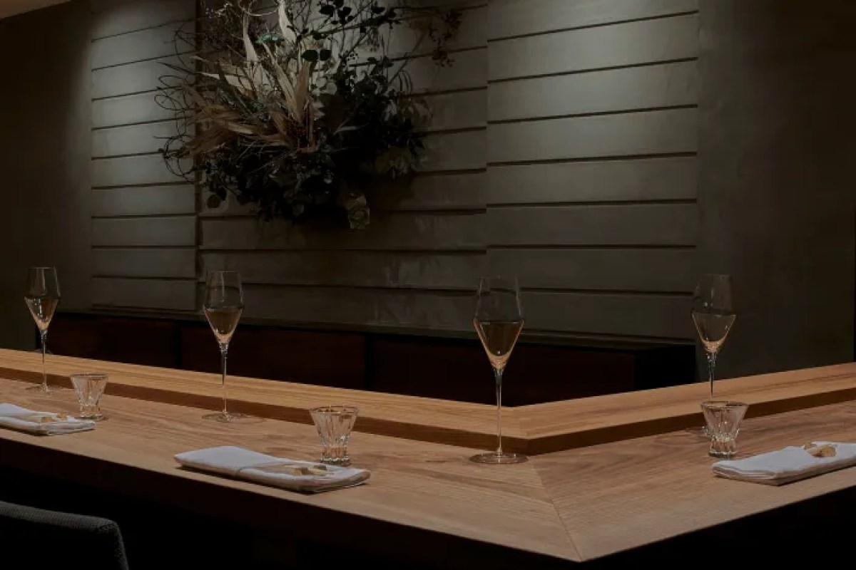 Empty wooden sushi bar counter set with wine glasses, napkins and a dried floral arrangement on the wall