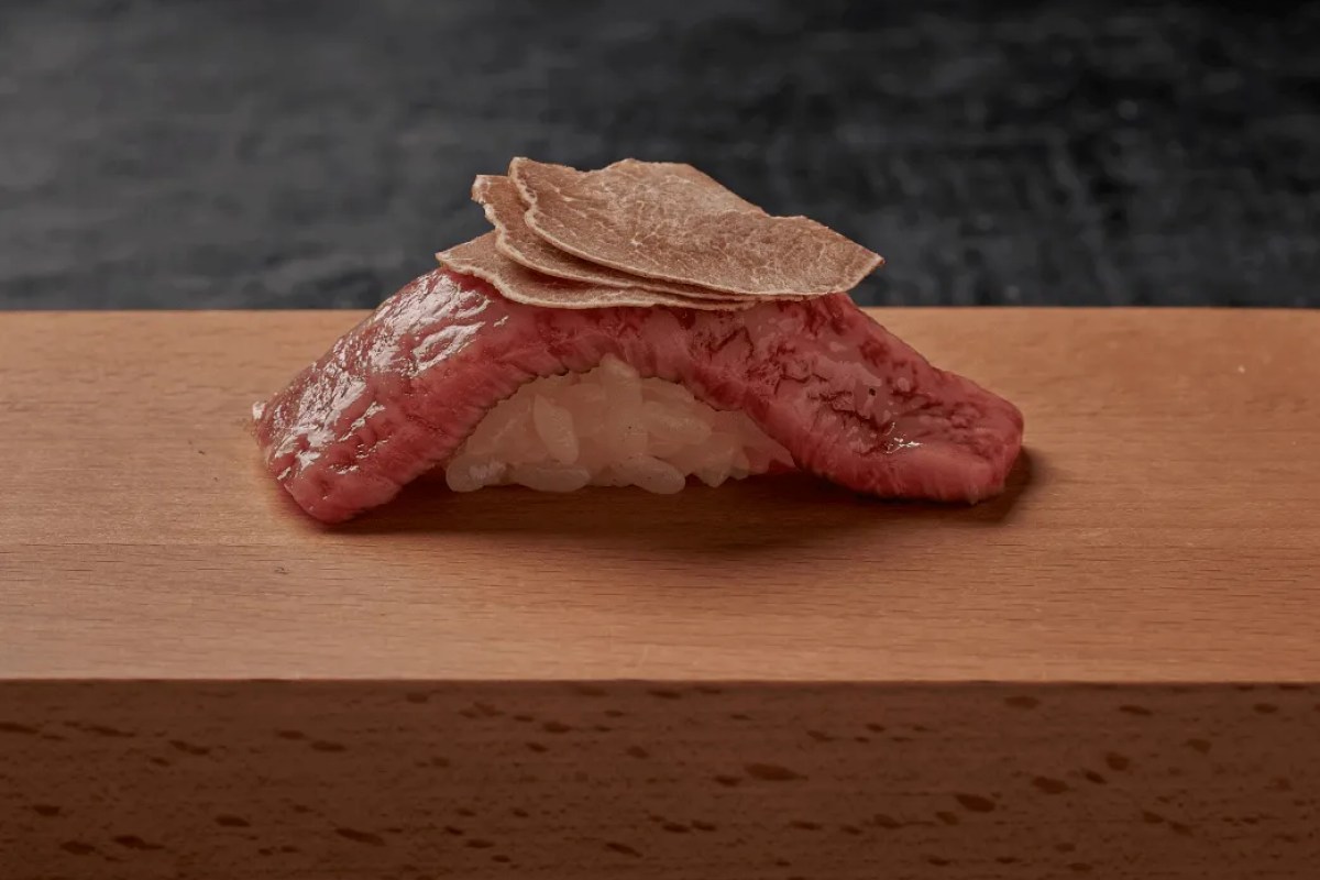 Wagyu beef nigiri topped with shaved truffle on a wooden counter