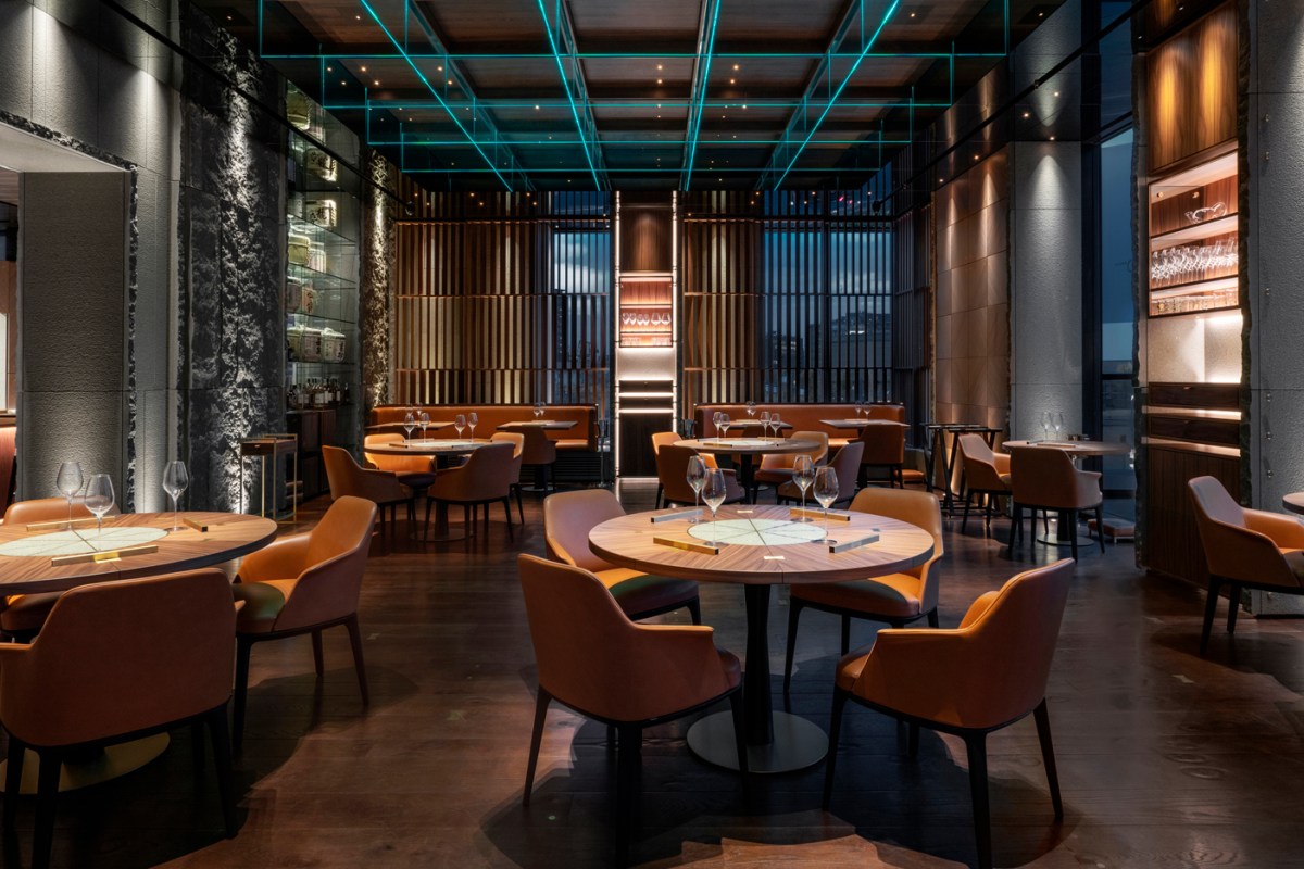 Modern dining room with round wooden tables, orange chairs, and teal neon ceiling lights at IYO Kaiseki