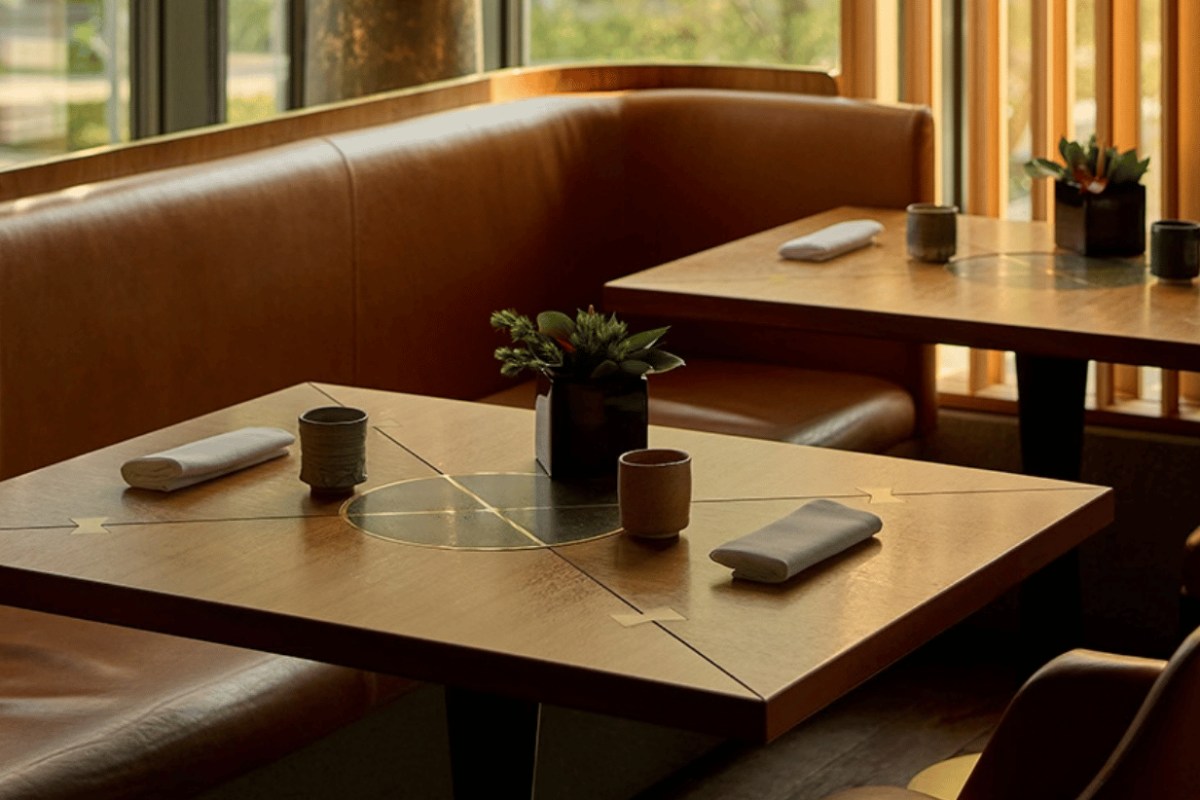 Bright dining area with leather booth seating and wooden tables set with napkins and small plants
