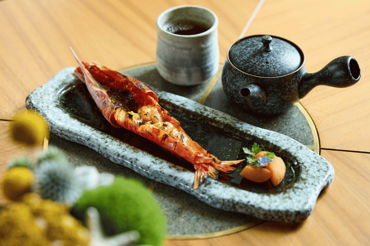Grilled langoustine served on a stone plate with tea cup and teapot, garnished with herbs