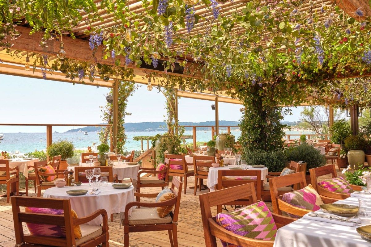 Restaurant terrace under a flower-draped pergola with set tables and sea view
