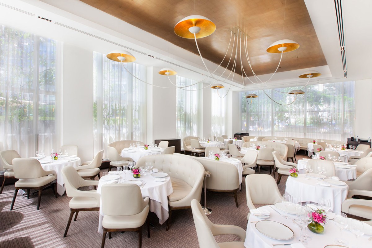 Spacious dining room with gold ceiling accents, sheer curtains, and elegant table settings.