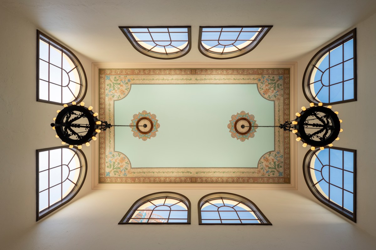 Ornate painted ceiling with arched windows and two wrought-iron chandeliers in the restaurant's dining room