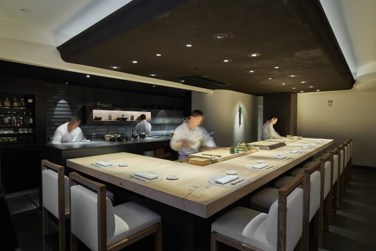 Sushi counter dining room with chefs working behind an open kitchen, wooden bar seating.