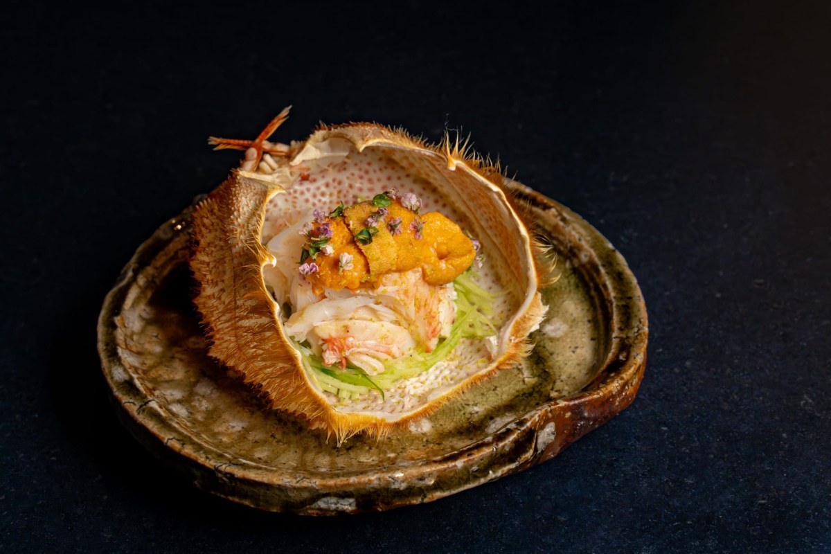 A crab shell dish filled with seafood, uni and edible flowers on a ceramic plate.