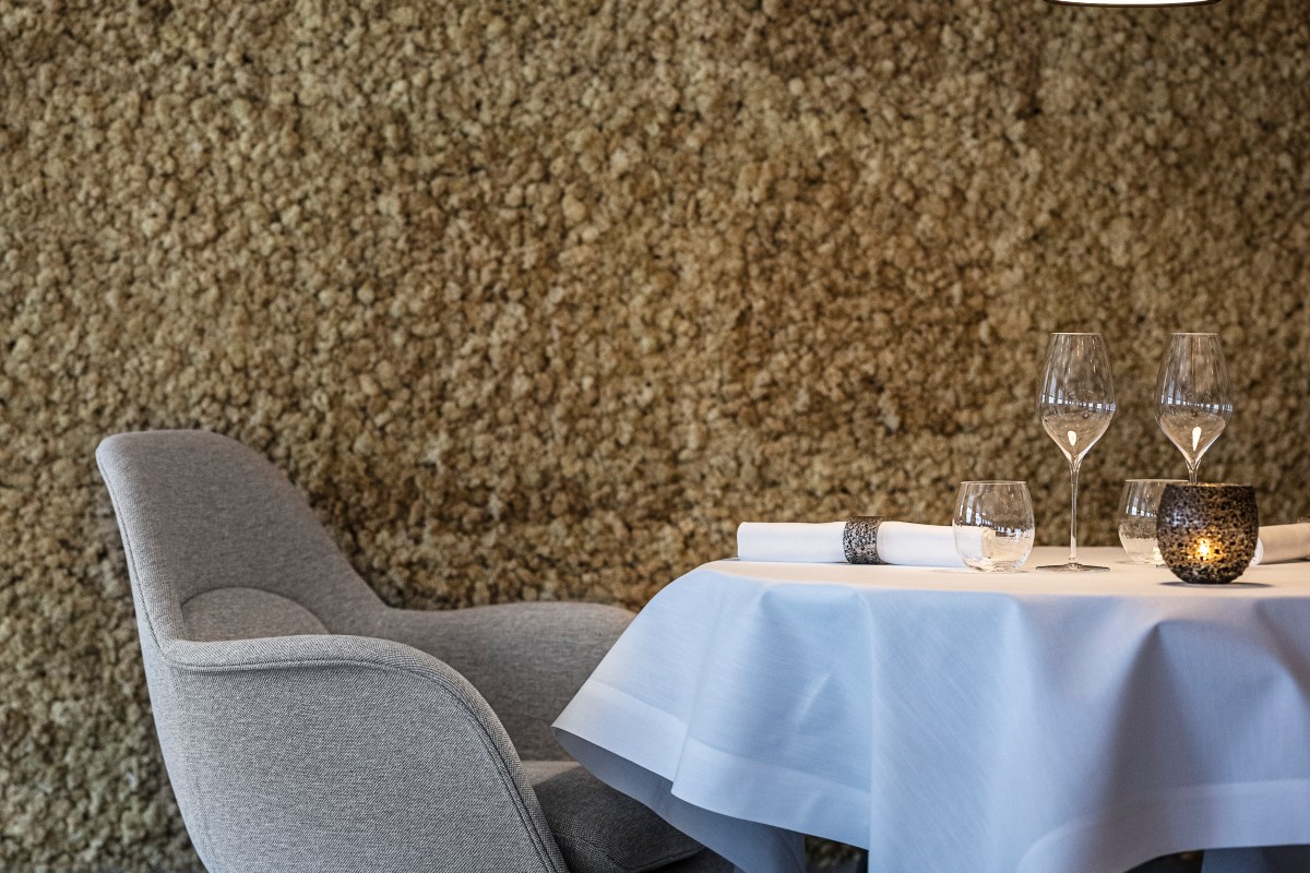 Dining room corner with upholstered chair, textured wall, and elegantly set table with wine glasses and candle