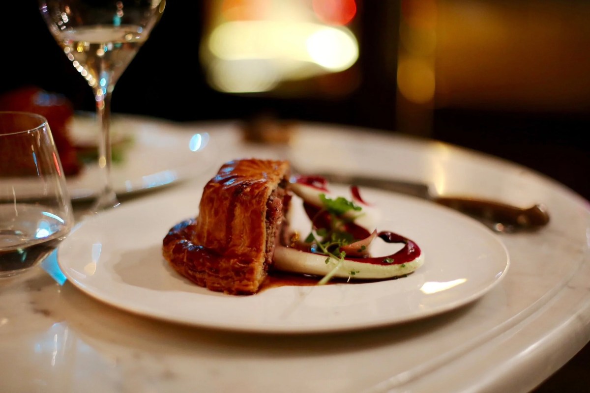 Plated pastry-wrapped dish with purple sauce on a white plate at a marble table