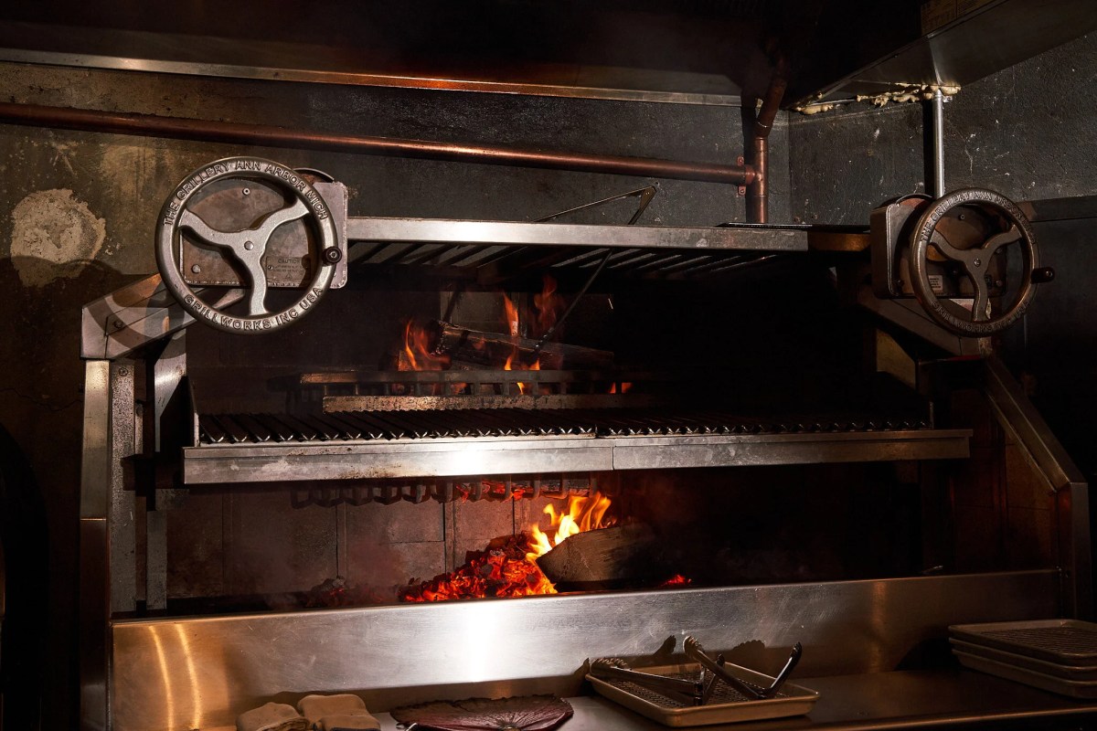 Open flame grill with fire and smoke inside restaurant kitchen