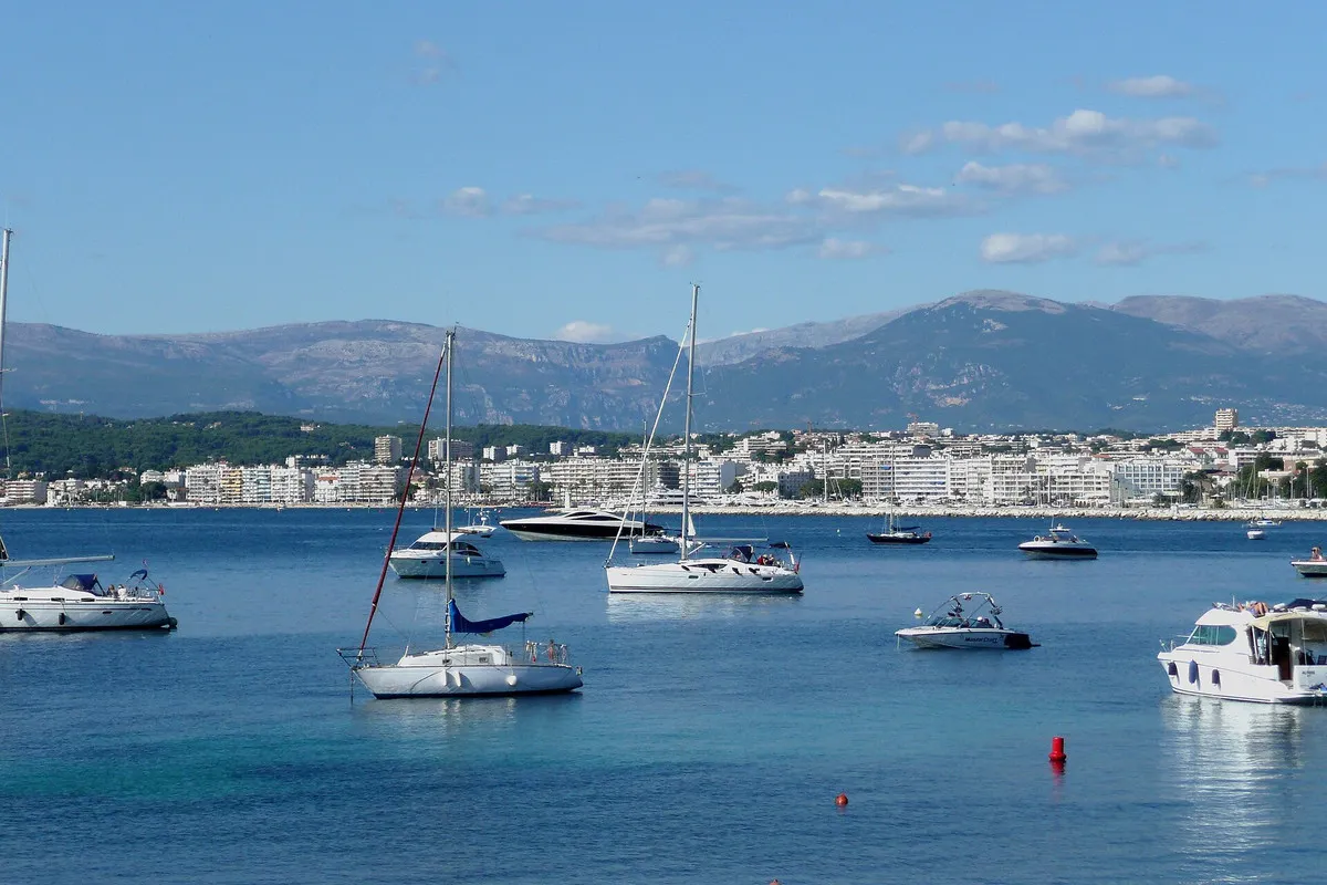 Yachts moored in the bay of Juan-les-Pins, seen from Cap d'Antibes, with the town and mountains behind